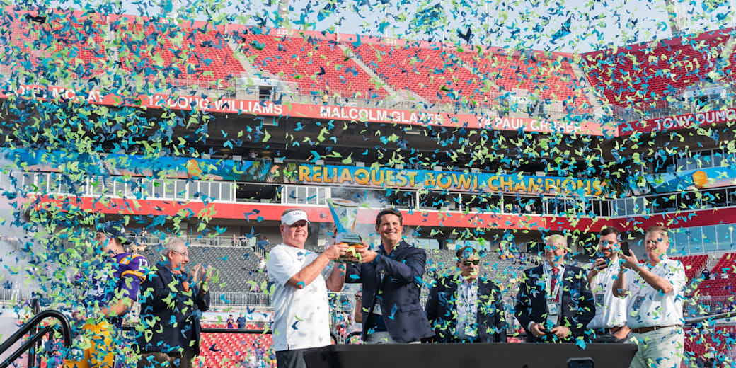 Confetti falls as the winning team lifts the ReliaQuest Bowl trophy on stage