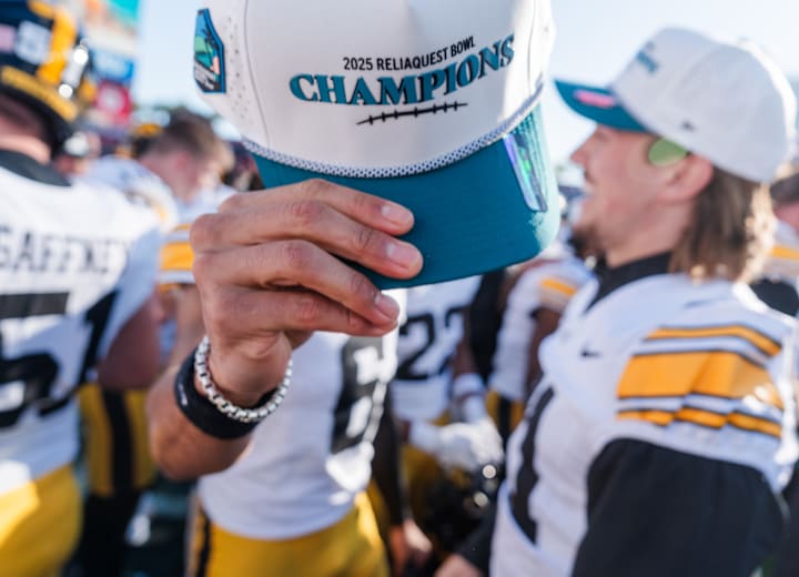 An Iowa player holds up a 2025 ReliaQuest Bowl Champions hat after the game